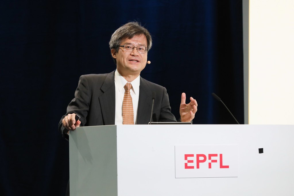 スーツにメガネの天野浩さんが、EPFLと書かれた白い演台の前で、手ぶりをまじえて話している