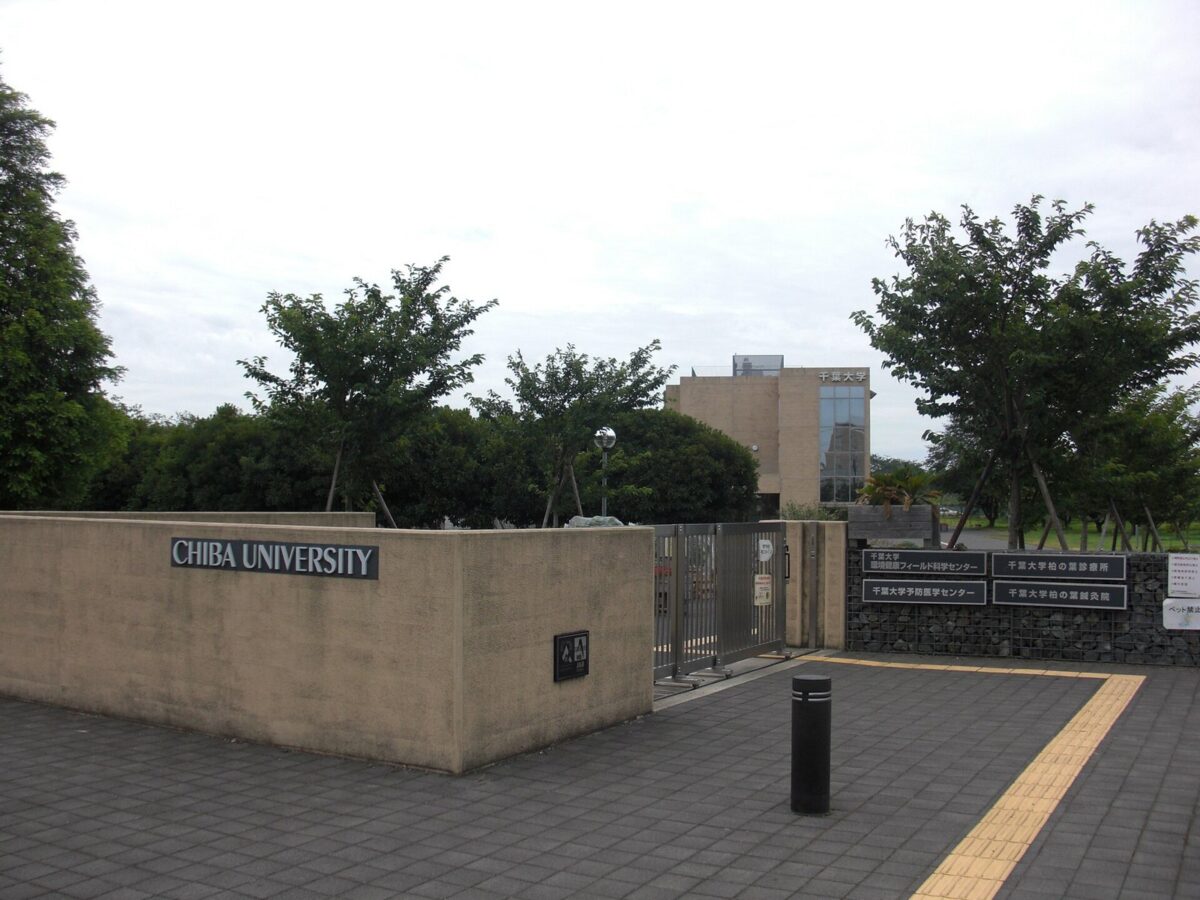 CHIBA UNIVERSITY と書かれた低いコンクリートの塀と門。奥に木々と建物が見える