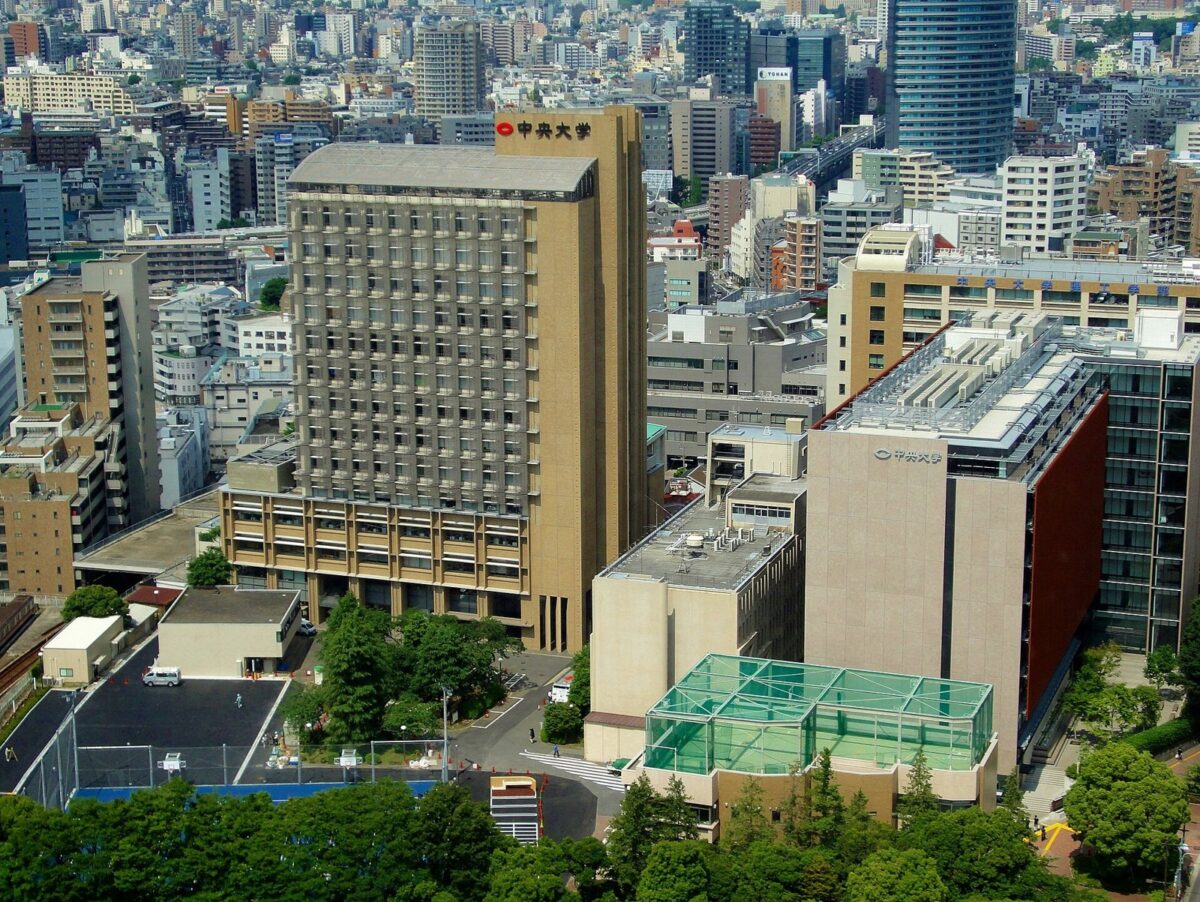 高いビルが並ぶ街の中に建つ大学のキャンパスを上から見た写真。茶色の高い建物の上に「中央大学」の文字があり、右の建物には「中央大学理工学部」と書かれている
