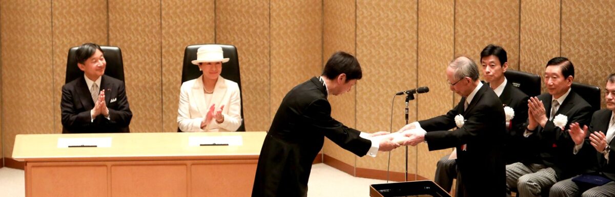 式典の会場で、天皇・皇后両陛下が拍手で見守る中、藤田先生が日本学士院の院長から賞を受け取っている