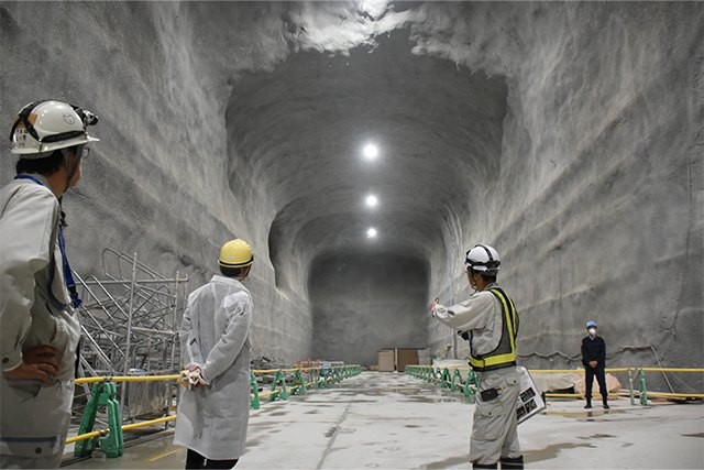 白い岩をくりぬいた、トンネルのような巨大な地下の空洞。ヘルメットをかぶった人たちが奥を見ている