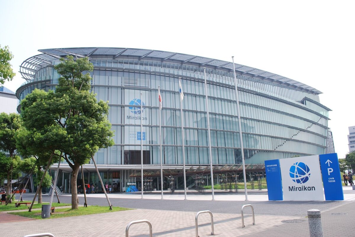 ガラス張りの丸い大きな建物。手前に「Miraikan」の看板と木がある