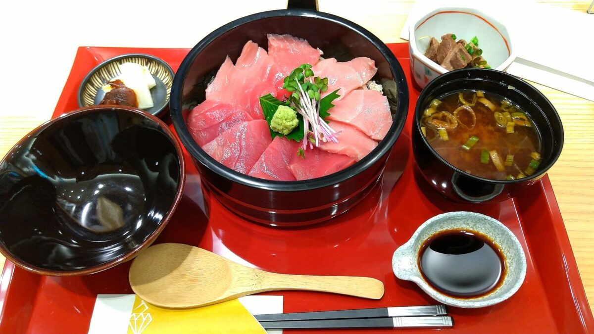 赤いお盆の上に、マグロの切り身をたっぷりのせた器と、みそ汁・小鉢・しょうゆ皿が並んでいる