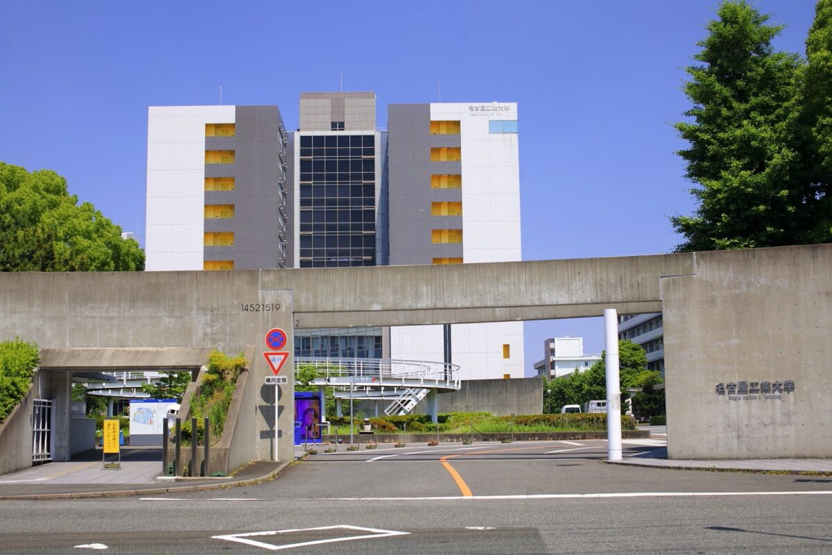 コンクリートの門の向こうに、白と灰色の高い校舎が建っている大学の正門