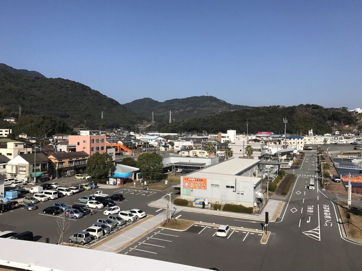 建物の上から見た、山を背にした港町の駐車場と町並み