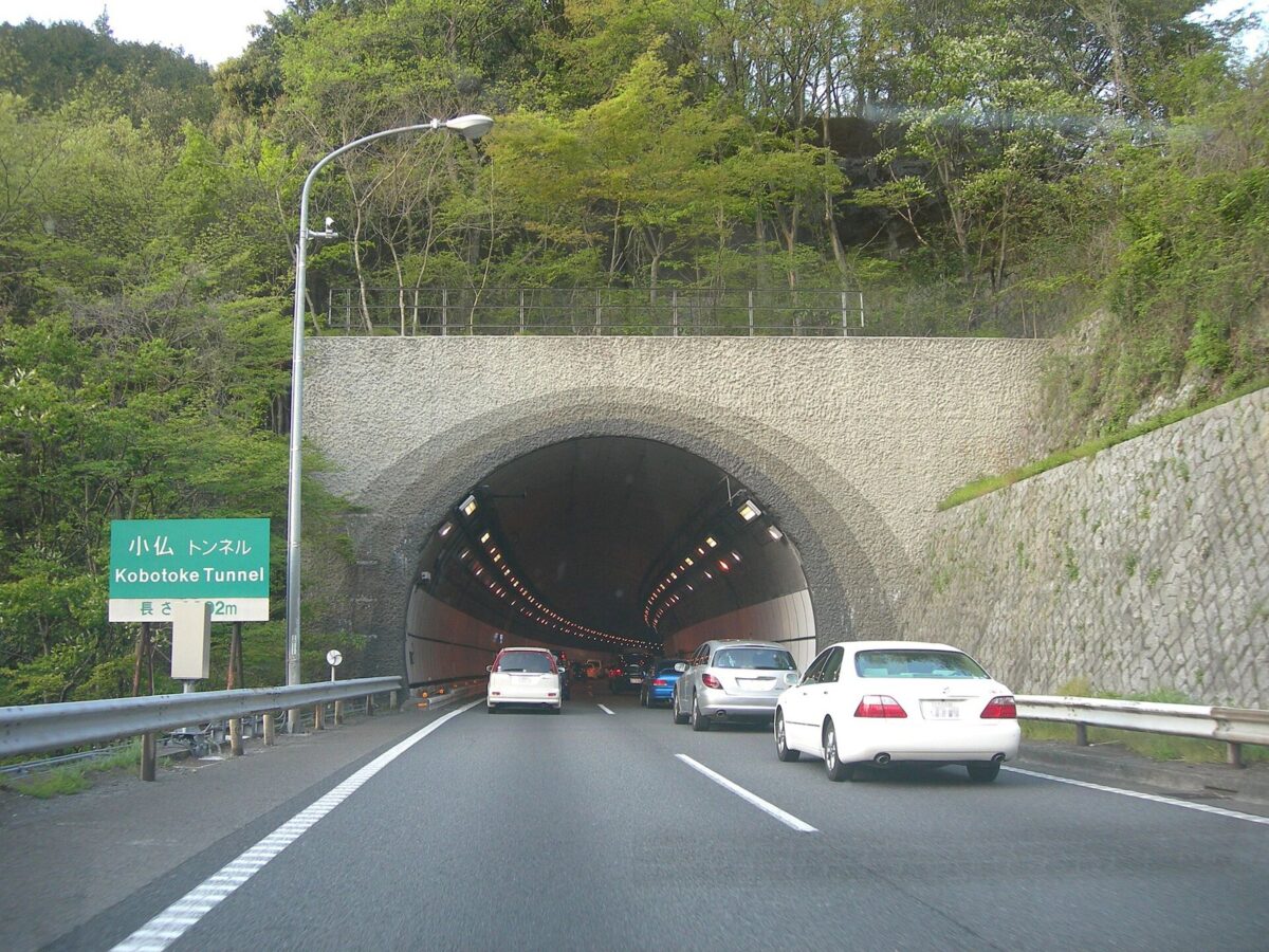 山の斜面に開いた高速道路のトンネルの入口。車が何台かトンネルへ向かって走っている