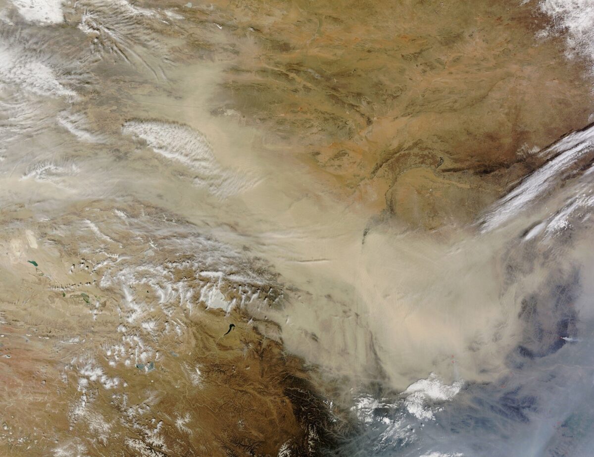 茶色い大地の上を、黄土色の砂ぼこりの帯が風に流されて広がっている衛星写真