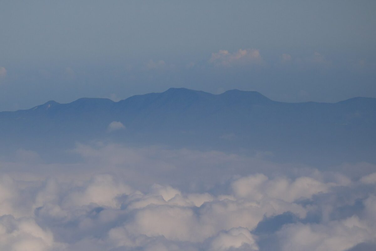 山の上から見下ろした一面の白い雲。雲の向こうに、遠くの山なみが青くかすんで見える