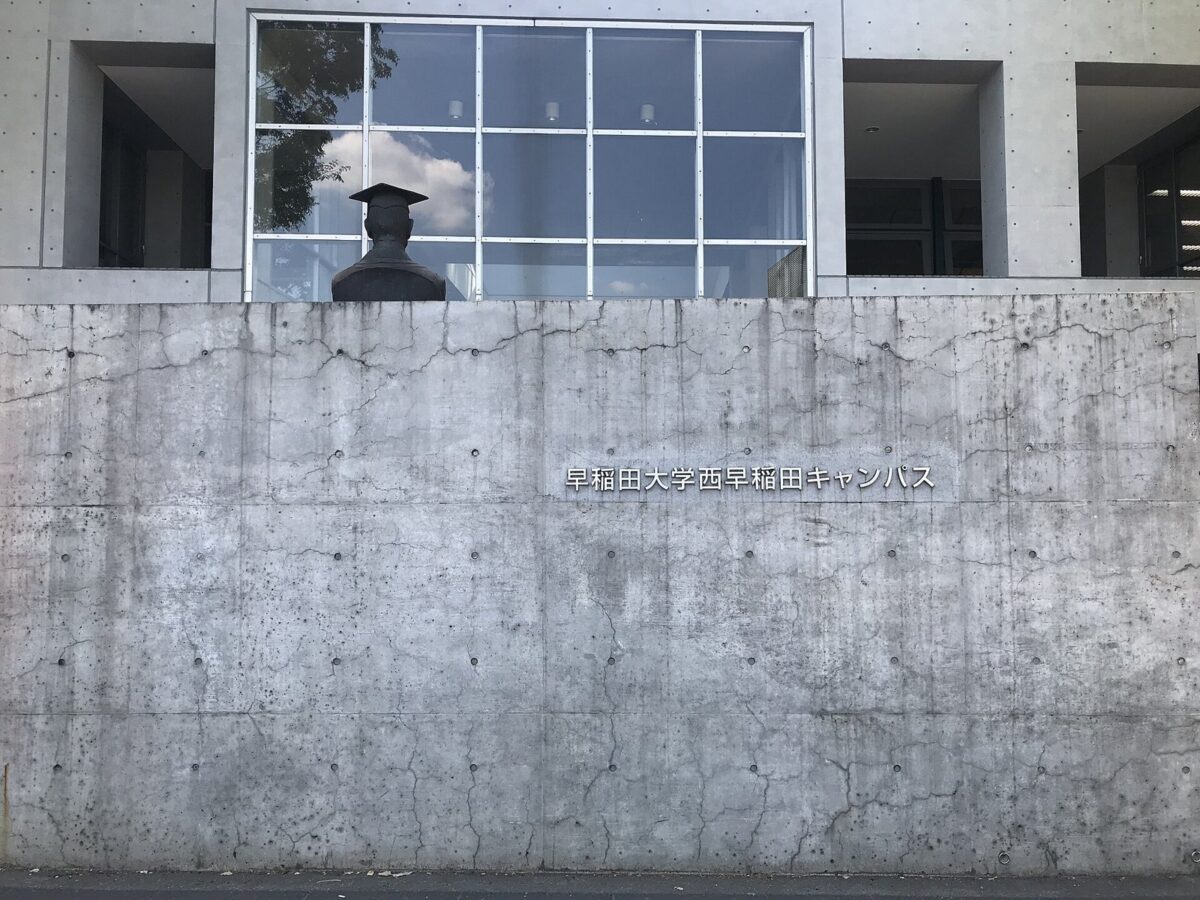 打ちっぱなしのコンクリートの壁に「早稲田大学西早稲田キャンパス」の文字がある、大学の門