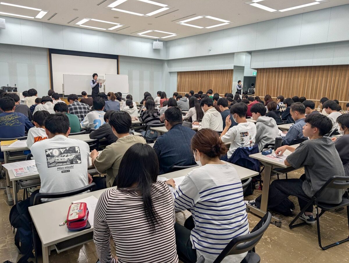 会場の前で話す大岩先生と、ほぼ満席の生徒たち