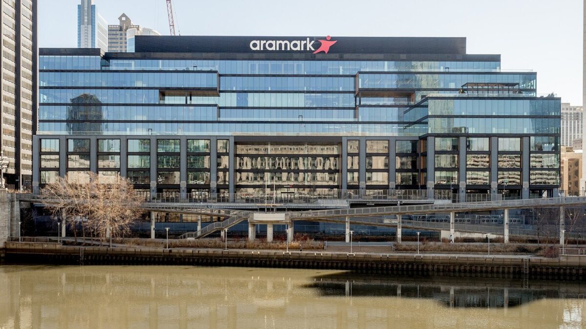 晴れた日、川の向こうに建つ、ガラス張りの横に長いオフィスビル。屋上に赤い星の付いた「aramark」の看板がある