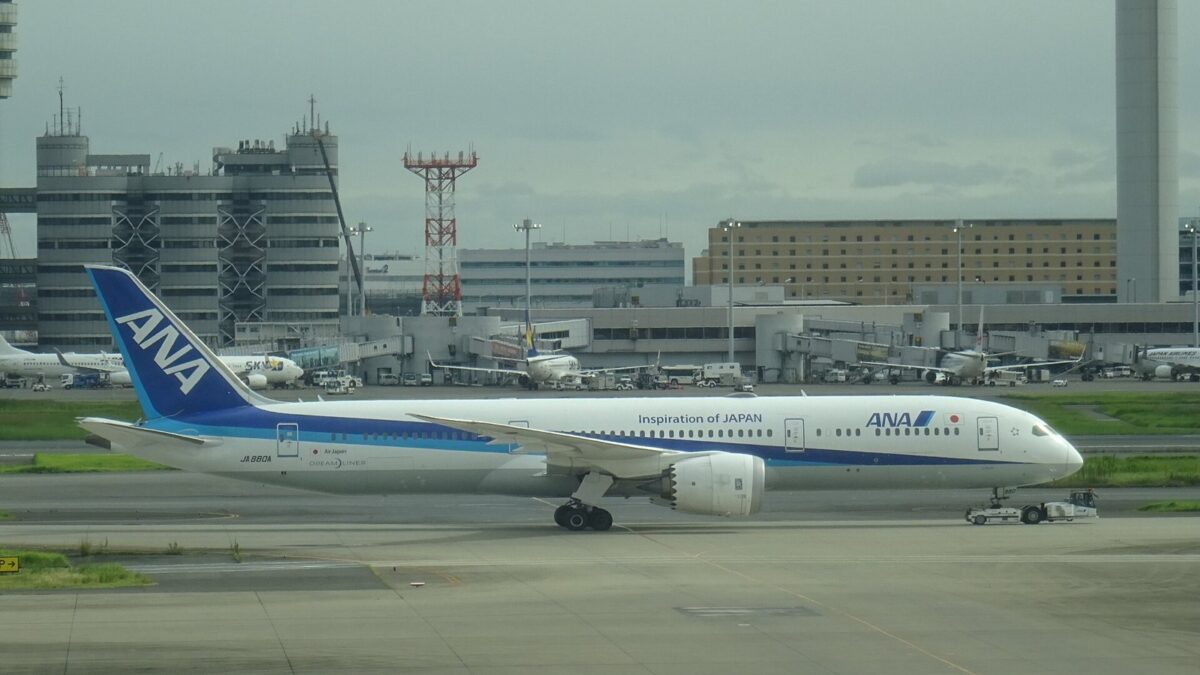 羽田空港の誘導路を走る、白い胴体に青い尾翼のANAの旅客機。奥に空港の建物と管制塔