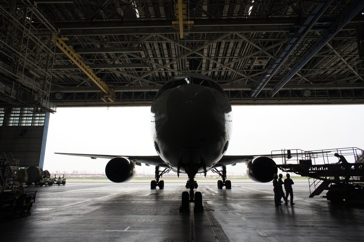 大きな格納庫の中に止まった旅客機を正面から見た写真。機体の横で整備の人が作業している