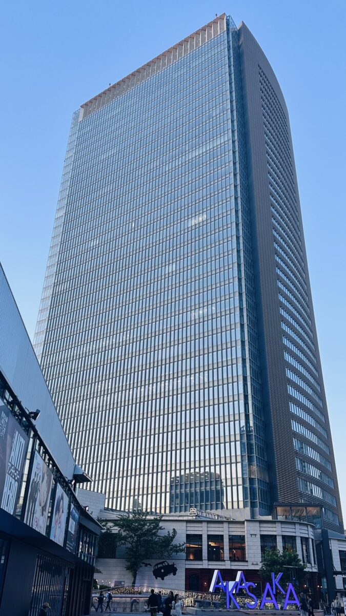 夕方の空の下に立つ、縦の線が入ったガラス張りの高層ビル