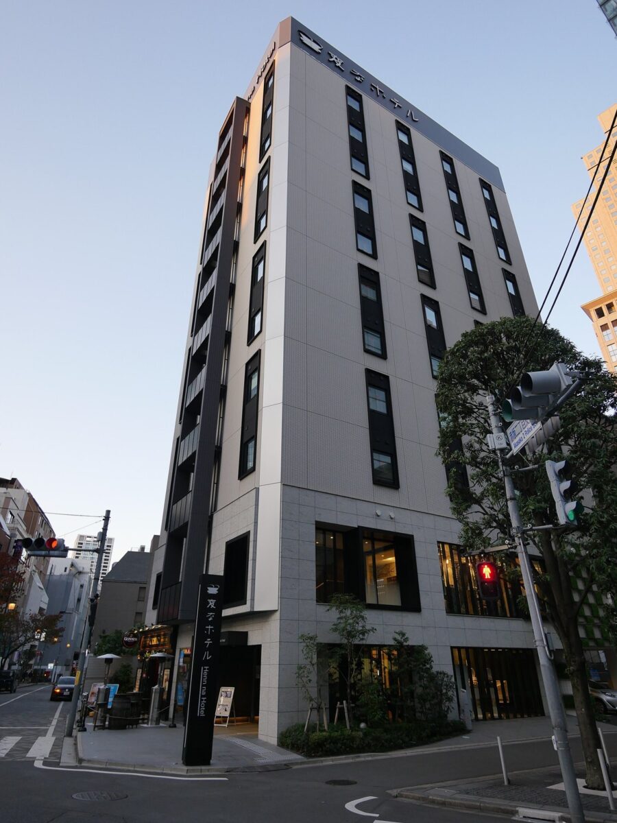 夕方の東京の街角に建つ、細長い10階建てくらいの白っぽいホテルの建物