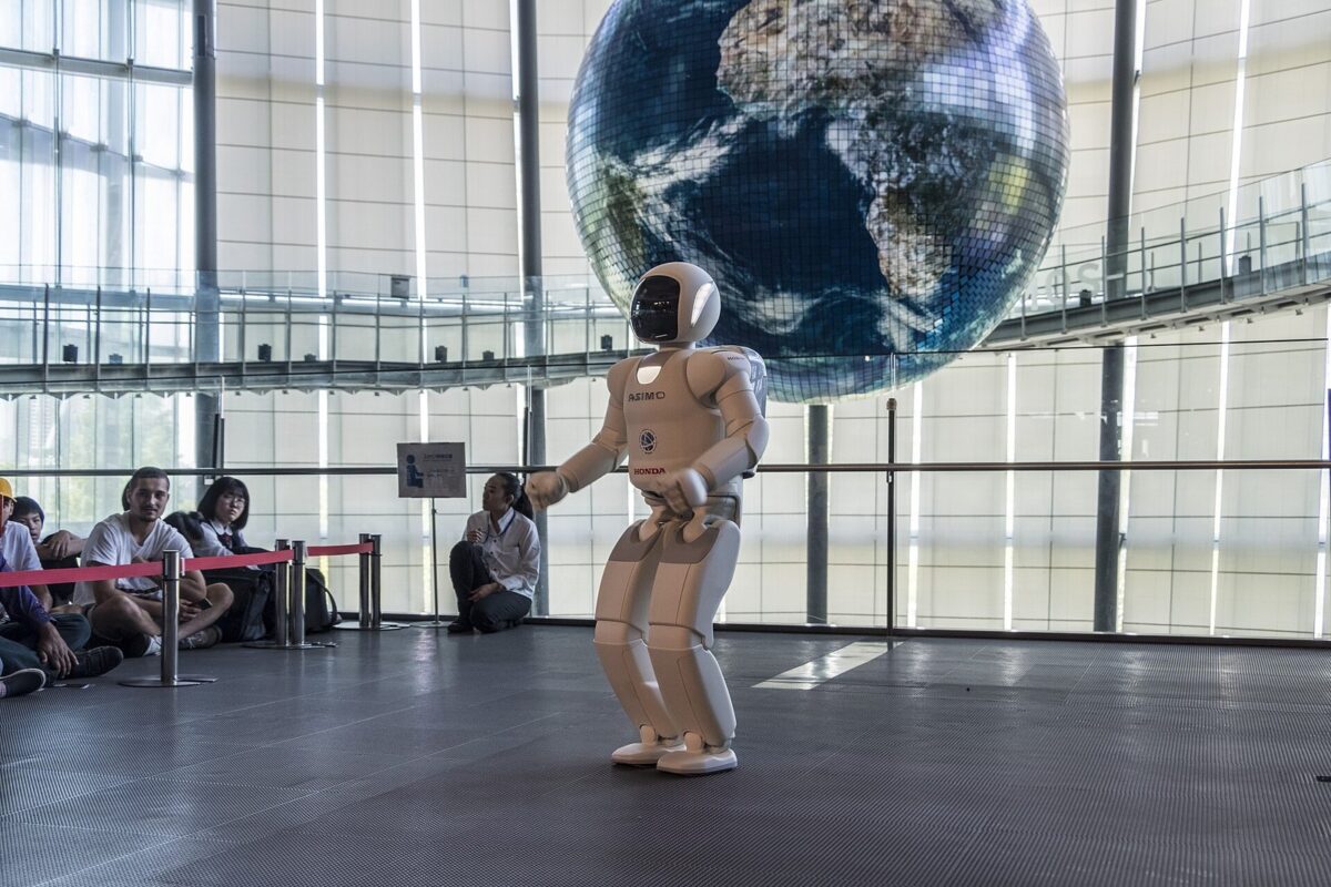 大きな地球の模型の下で、白い人の形のロボットがひざを曲げて立っている
