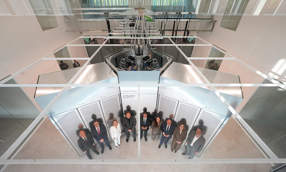 吹き抜けの上から見下ろした、銀色の壁に囲まれた大きな機械と、その前に並ぶスーツの人たち