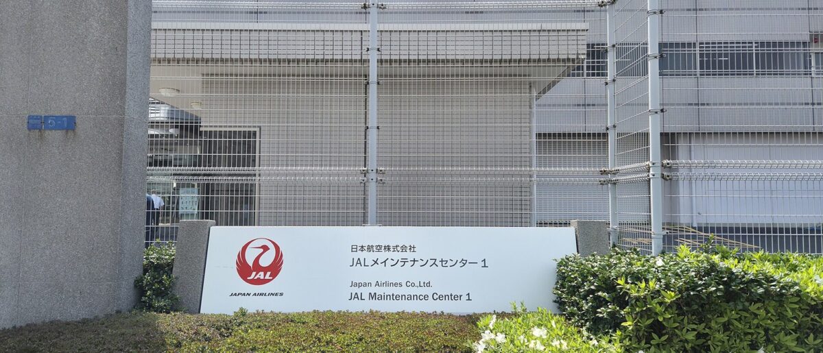 鶴のマークと「日本航空株式会社 JALメインテナンスセンター1」と書かれた看板と、その奥の灰色の建物