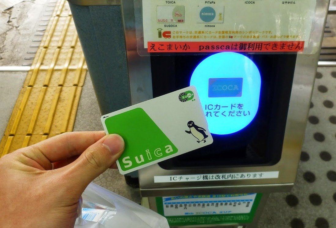 緑のSuicaのカードを手に持ち、青く光る改札機の読み取り部分にかざしている