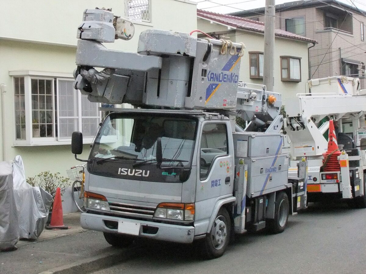 住宅街に止まった、腕を折りたたんだ白い高所作業車を前から写した写真
