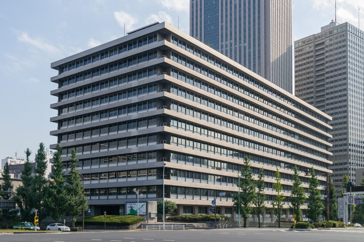 窓が横にずらりと並ぶ、灰色の10階建てほどの役所のビル。後ろに高層ビルが建っている