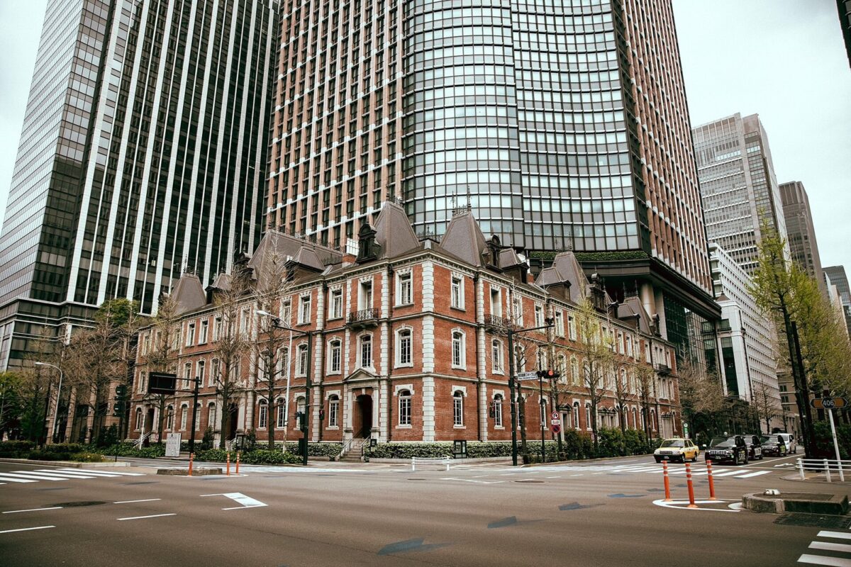 赤れんがの3階建ての洋館。うしろに、ガラス張りの高層ビルが2本そびえている