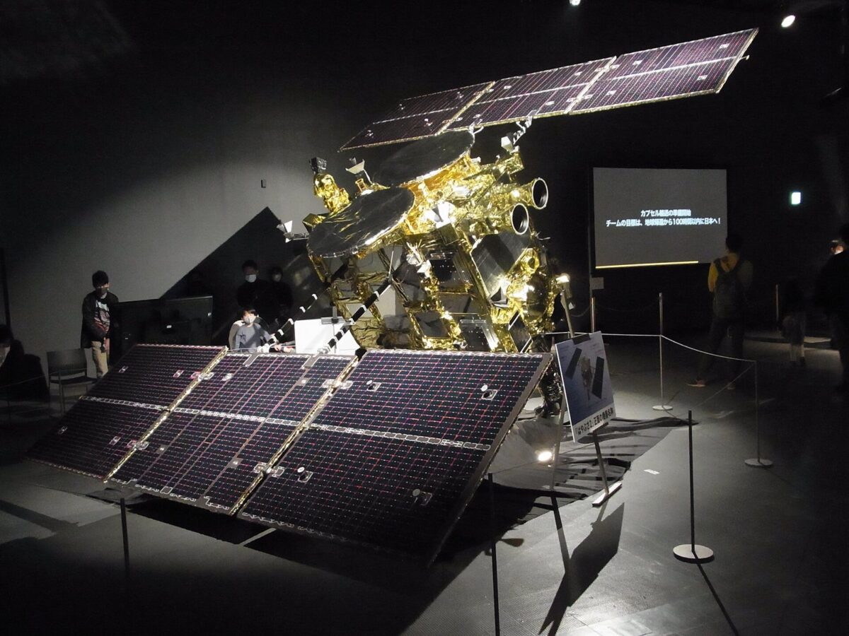 暗い展示室に置かれた、金色の箱の形の本体に、大きな太陽電池の板が広がった探査機の模型