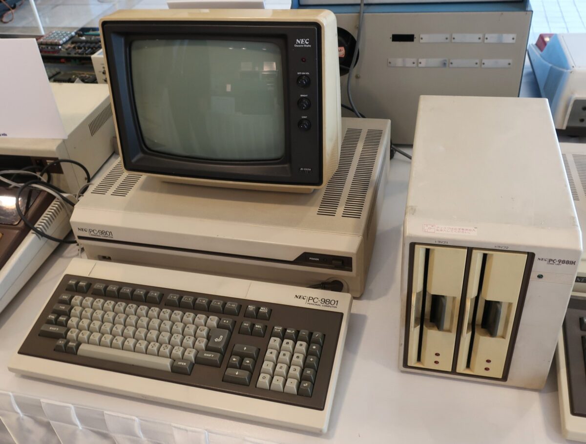 博物館に展示された、灰色の古いパソコンの本体とキーボード、白黒の画面、大きな箱型のフロッピーディスクの装置