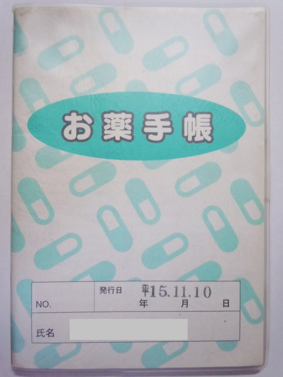 白地に水色のカプセルの絵がちりばめられた表紙に「お薬手帳」と書かれた、小さな冊子。名前の欄は隠してある