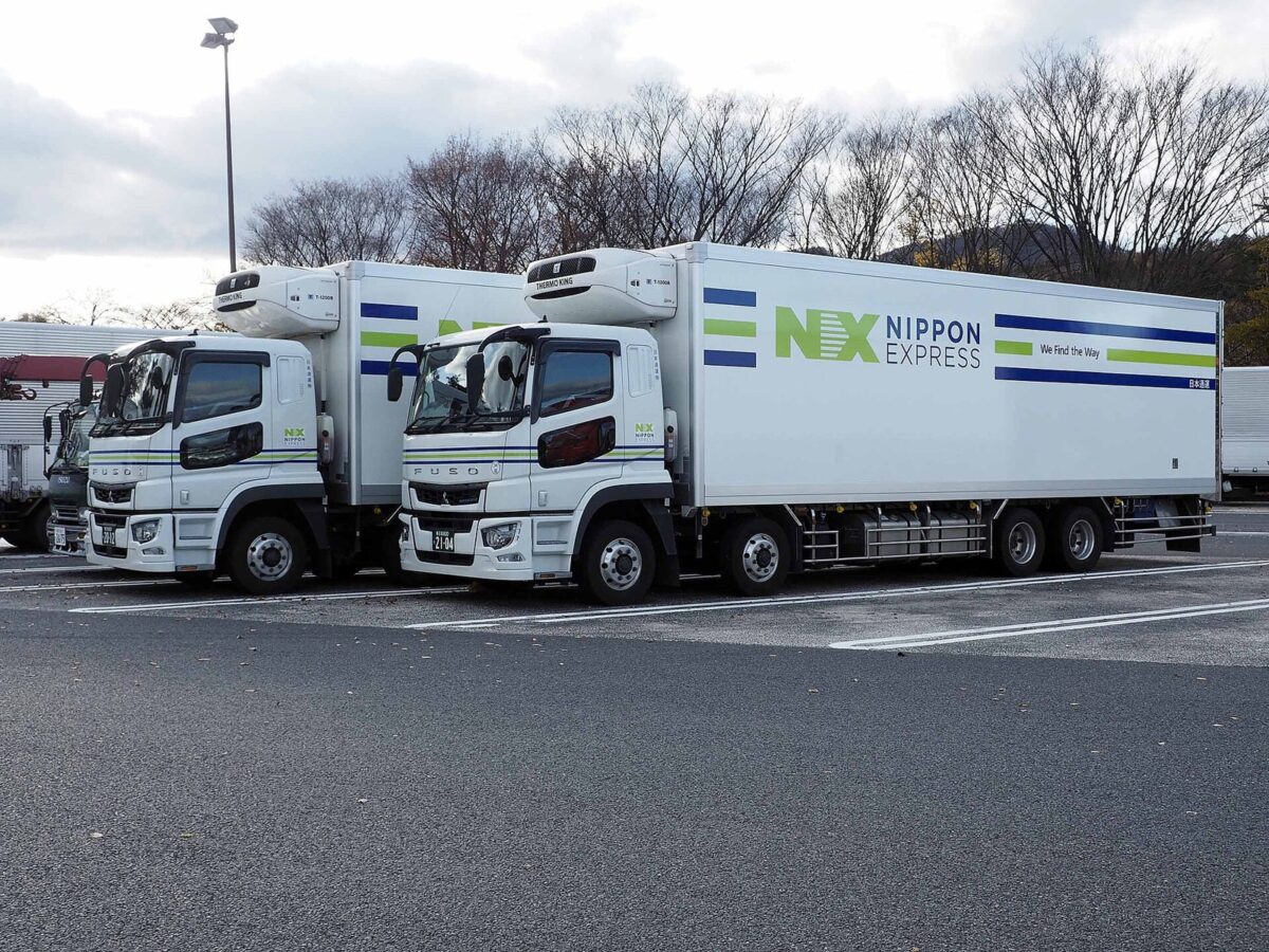 高速道路のサービスエリアの駐車場に、荷台が白い箱型で「NX NIPPON EXPRESS」と書かれた日本通運の大型トラックが2台並んで止まっている