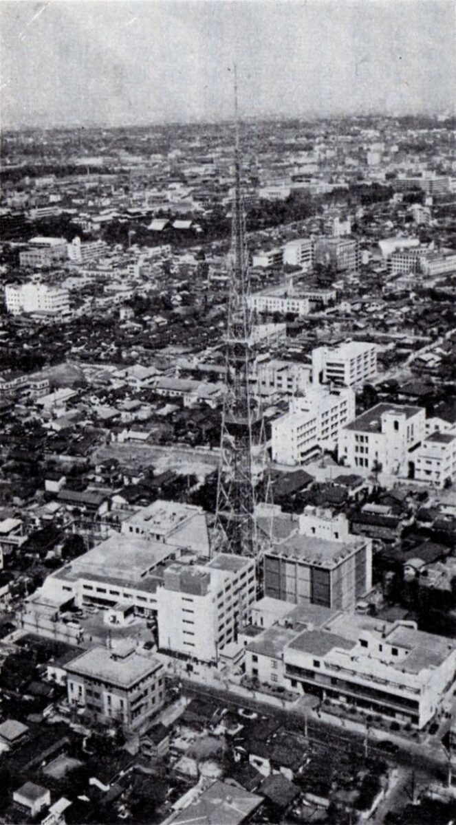 空から見た昔の白黒写真。家やビルが並ぶ街の中に日本テレビの本社の建物があり、その真ん中から高い鉄塔が伸びている