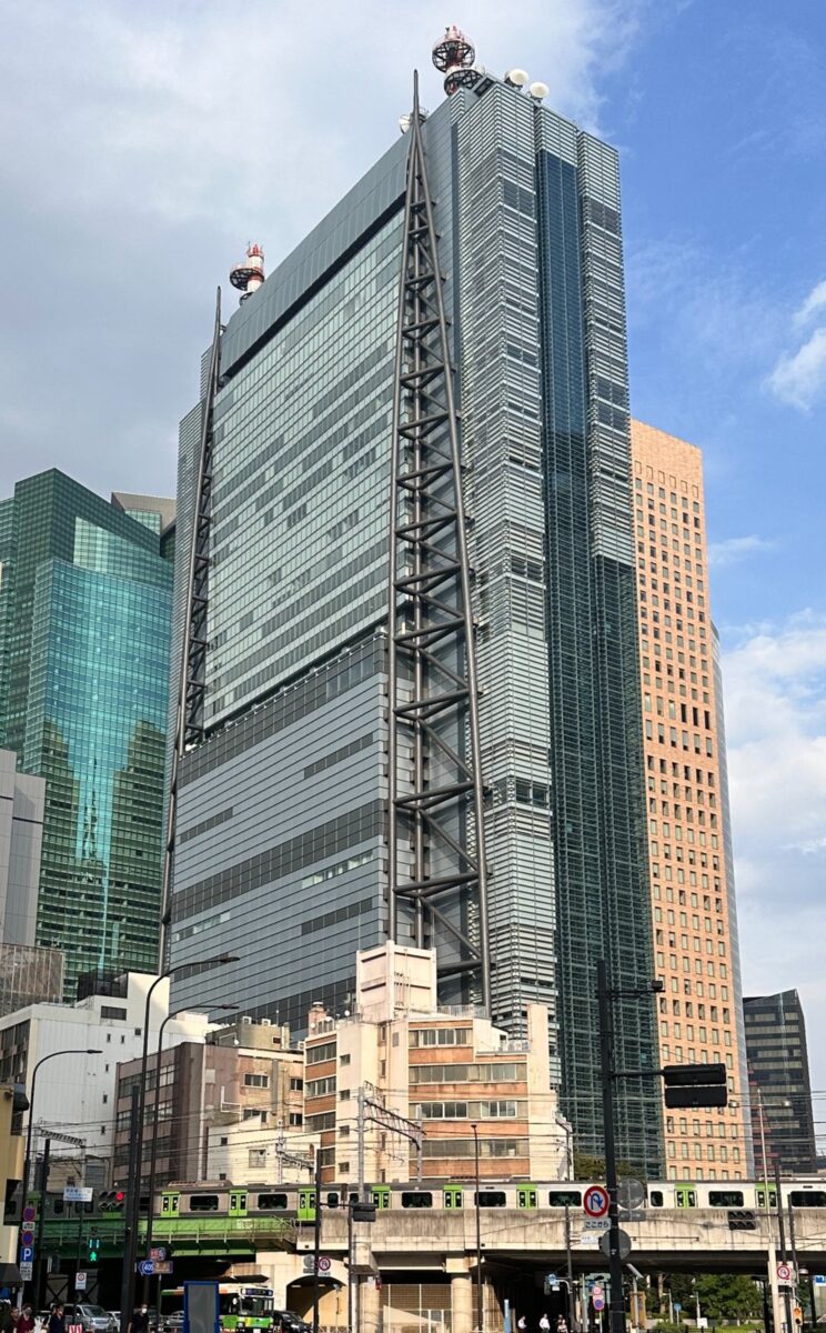 青空の下にそびえる、ガラス張りの高いビルの日本テレビタワーを見上げた写真