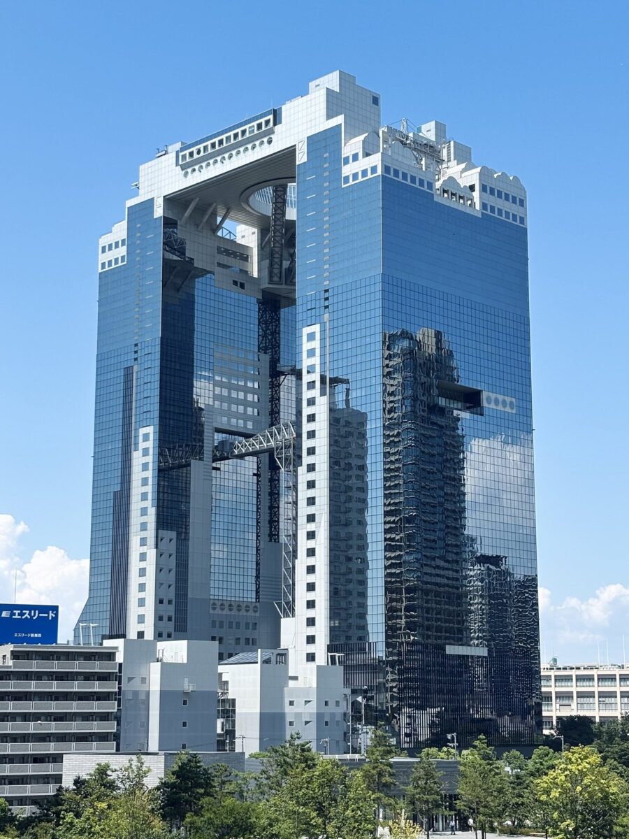 青空の下、2本の高層ビルが最上部の丸い空中の展望台でつながった、ガラス張りの大きなビルを見上げた写真