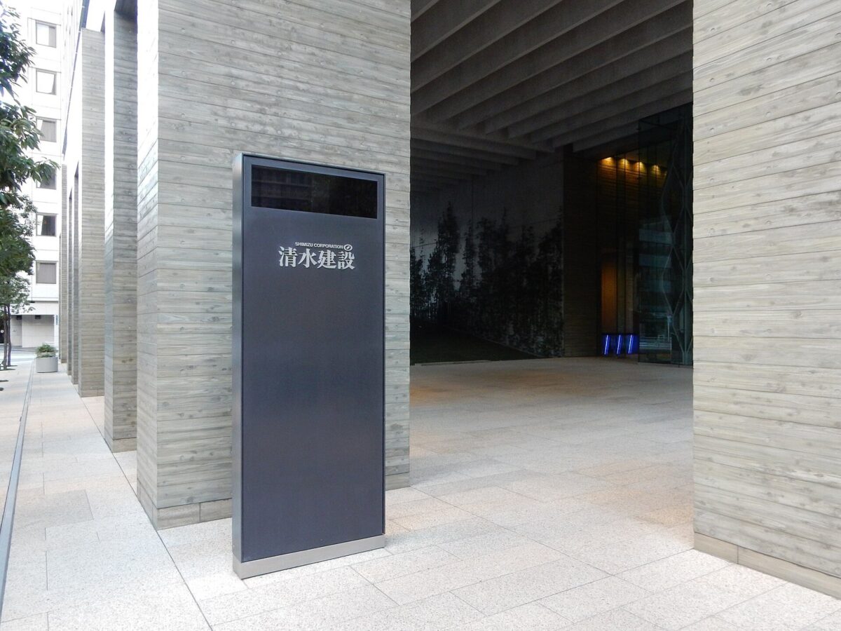 木目の模様が付いた太い柱が並ぶビルの入口と、「清水建設」と書かれた黒い案内板の写真