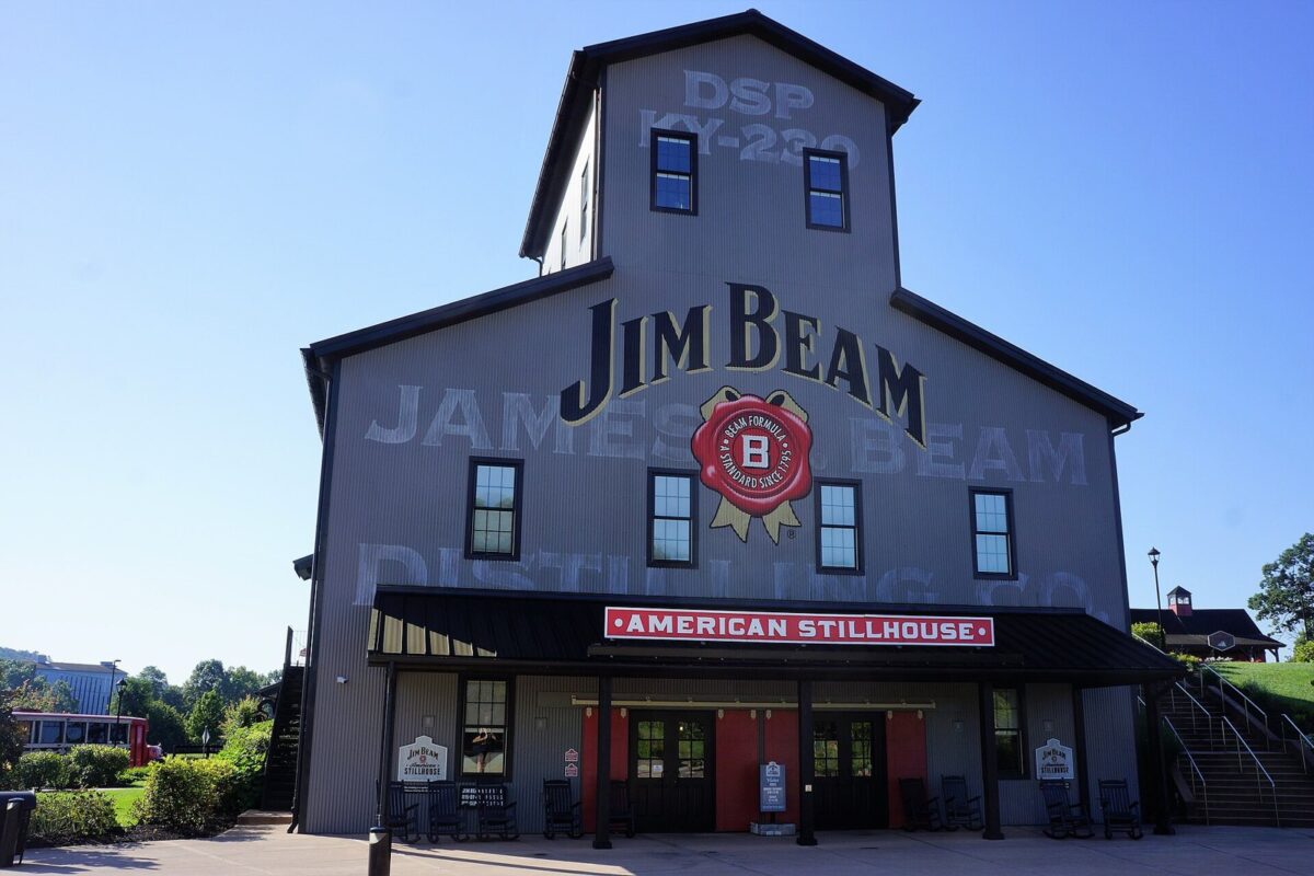 青空の下に建つ、灰色の板張りの納屋のような大きな建物。壁に「JIM BEAM」の文字があるアメリカのウイスキーの蒸溜所