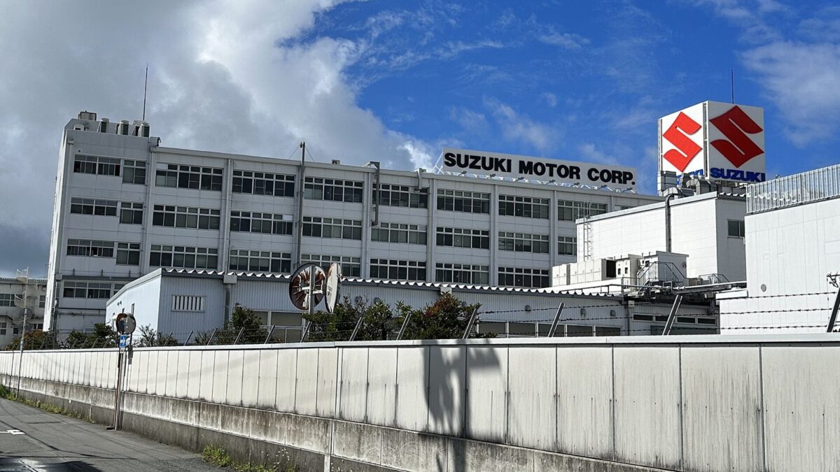 青空の下に建つ、横に長い白いビル。屋上に「SUZUKI MOTOR CORP.」の看板と赤いSのマーク