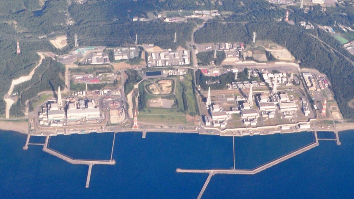 海に面した広い敷地に、四角い建物がいくつも並び、手前の海には防波堤が伸びている航空写真